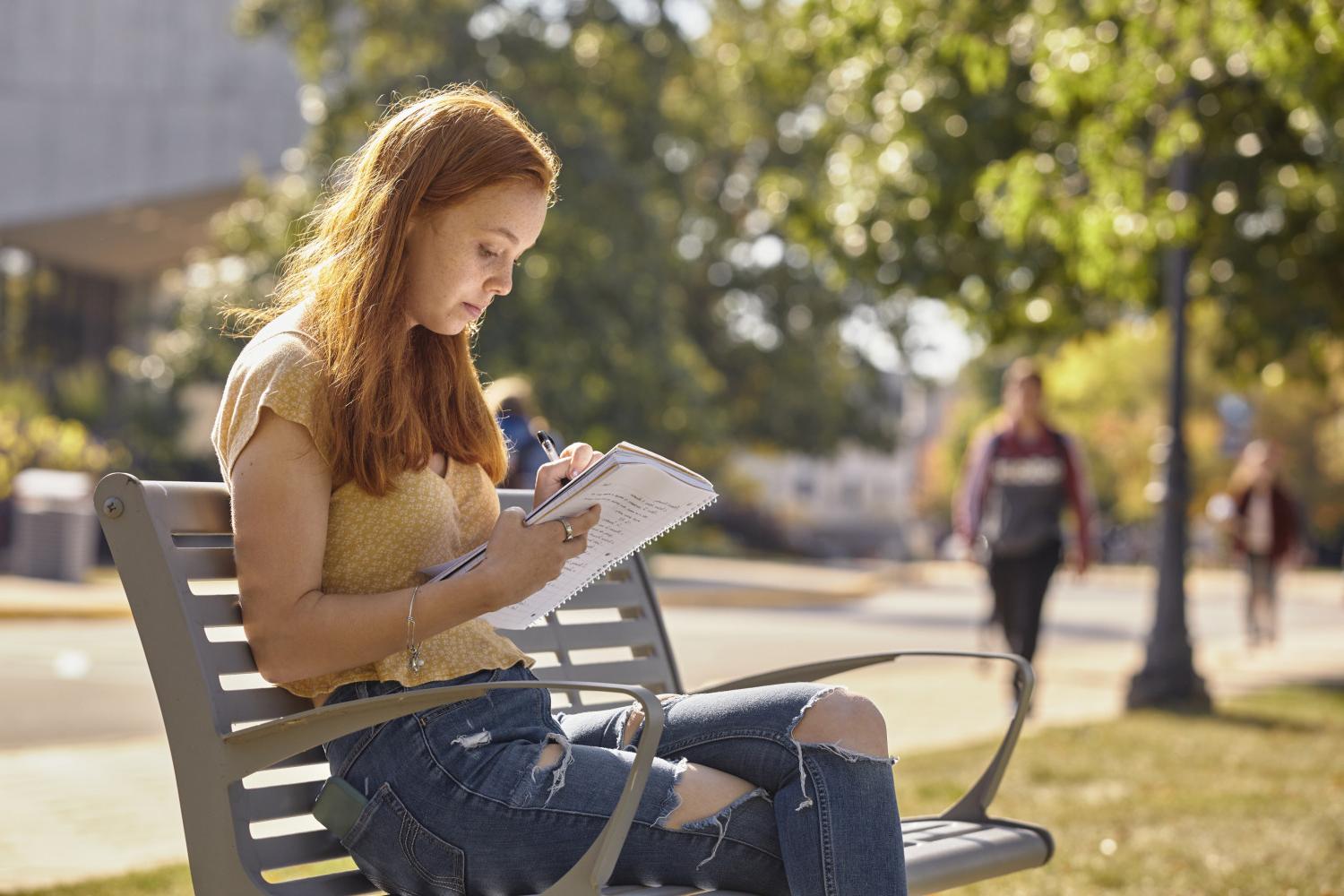 A <a href='http://61zn.lengyileng.com'>博彩网址大全</a> student reads on a bench along Campus Drive.